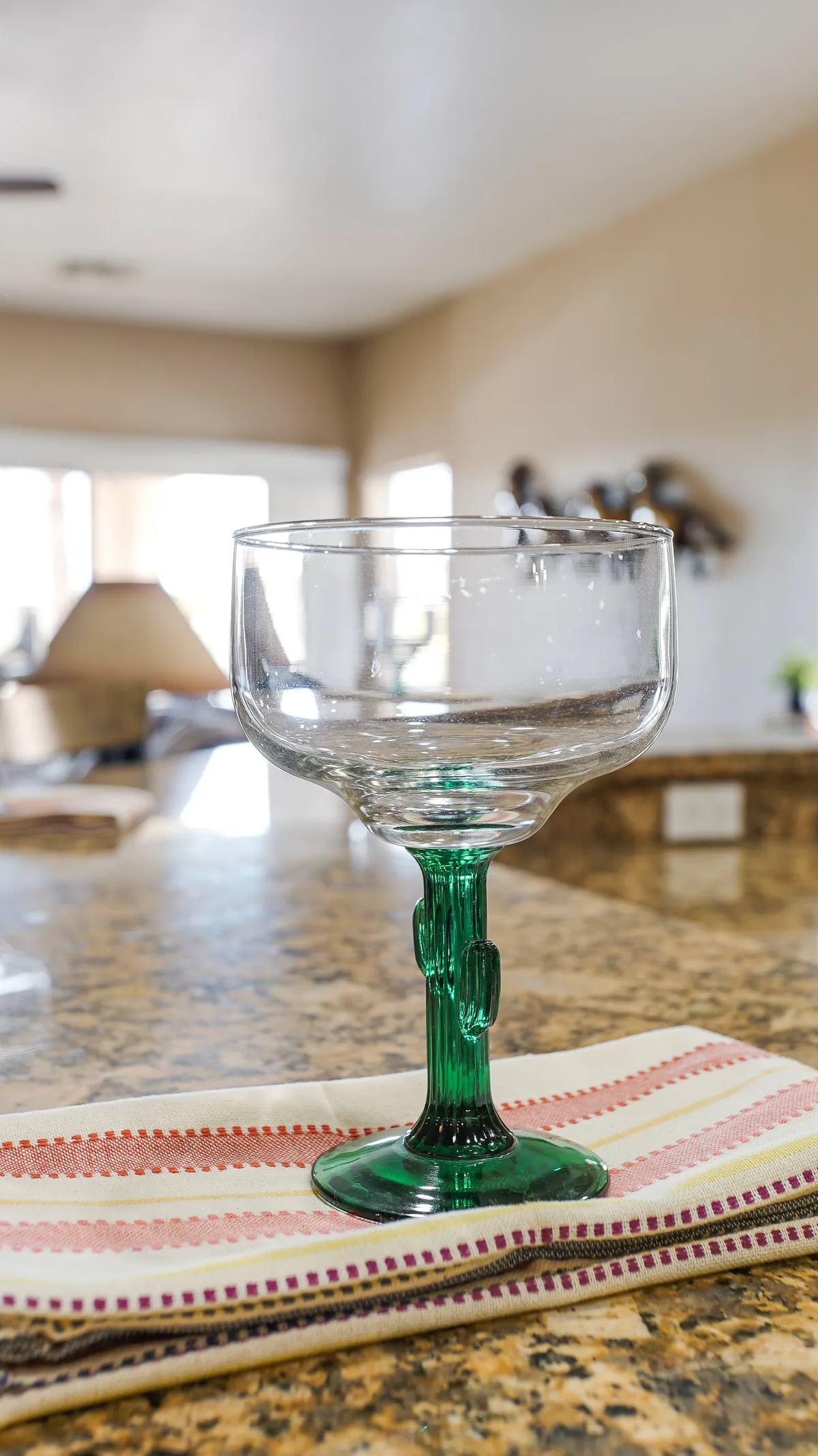 A cheerful kitchen countertop vignette featuring a green glass margarita glass, a striped kitchen towel, and a granite workspace, perfect for entertaining or relaxing with a drink while cooking.