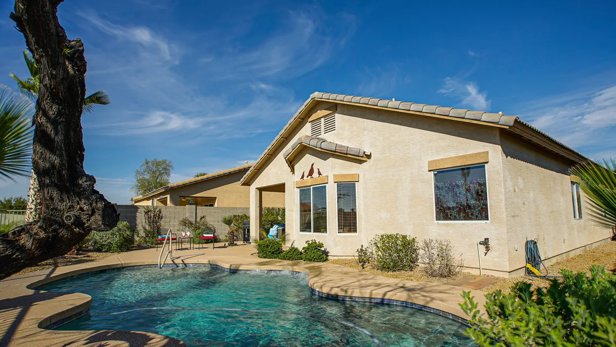 A vibrant exterior view of the home featuring a sparkling swimming pool, lush landscaping, and a clear blue sky. The inviting poolside area is ideal for relaxing after a round of golf, while the house facade hints at the comfort within.