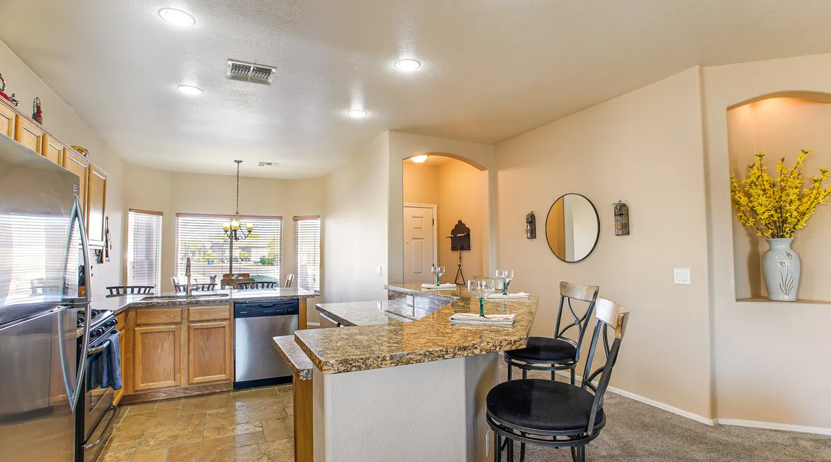 A welcoming kitchen scene with a polished granite countertop, modern stainless steel appliances, bar stools for casual dining, and a decorative vase adding a touch of warmth.