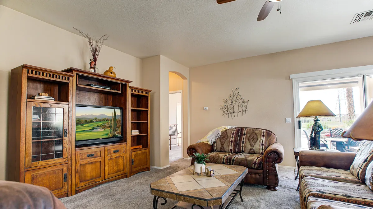 A cozy living room featuring a wooden entertainment unit, a coffee table, a couch adorned with decorative pillows, and a large window that offers scenic views outside. Natural light fills the space, enhancing the comfort and inviting atmosphere.