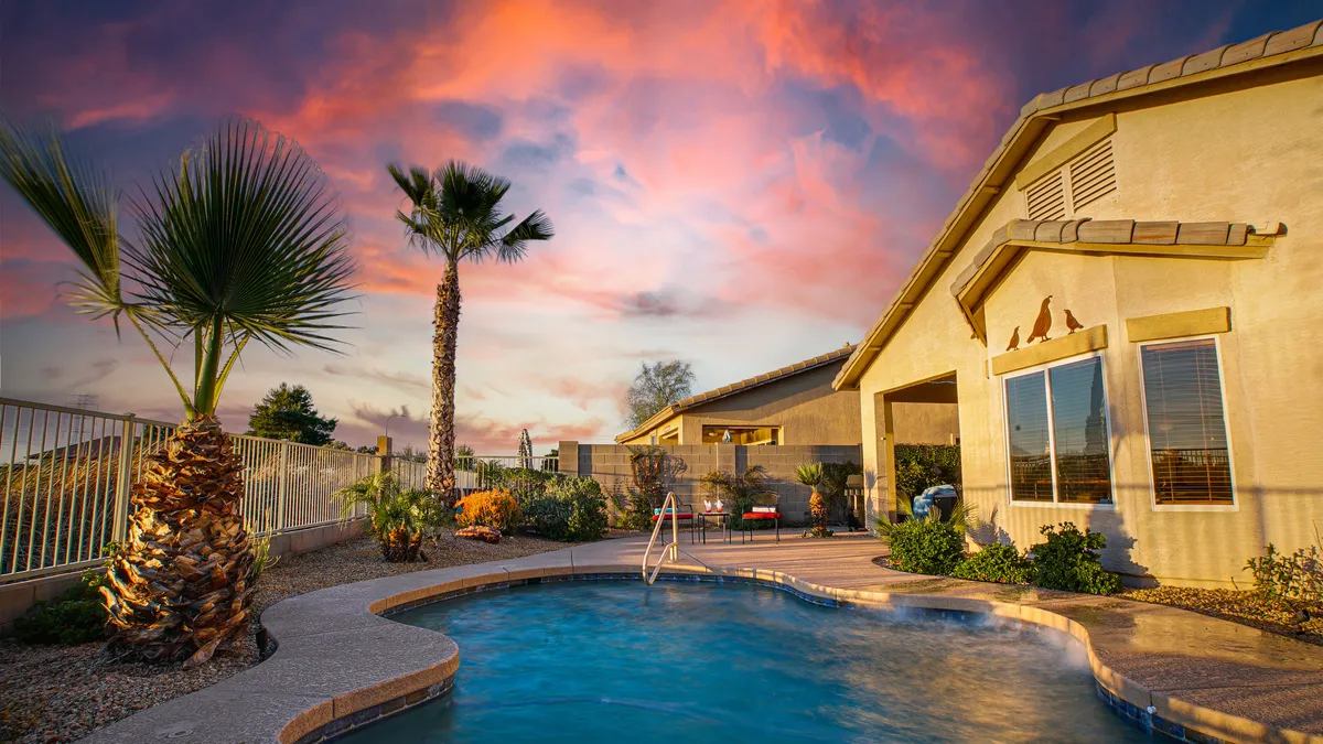 The exterior view showcases a tranquil swimming pool with palm trees, the house facade in the background, and a sky dappled with clouds. The scene invites outdoor enjoyment—swimming, barbecuing, or morning coffee by the pool.