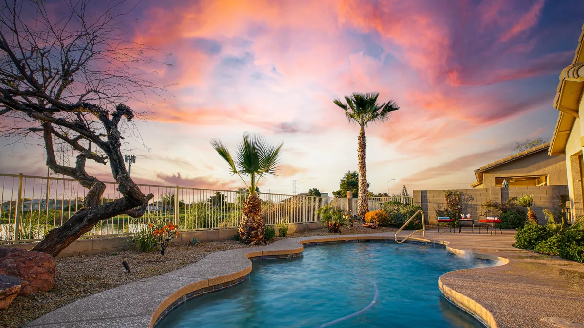 A serene backyard swimming pool bordered by graceful palms, with a vibrant sunset sky overhead. The setting is peaceful, perfect for relaxing by the water, stargazing, or gathering with friends after a day exploring Avondale.
