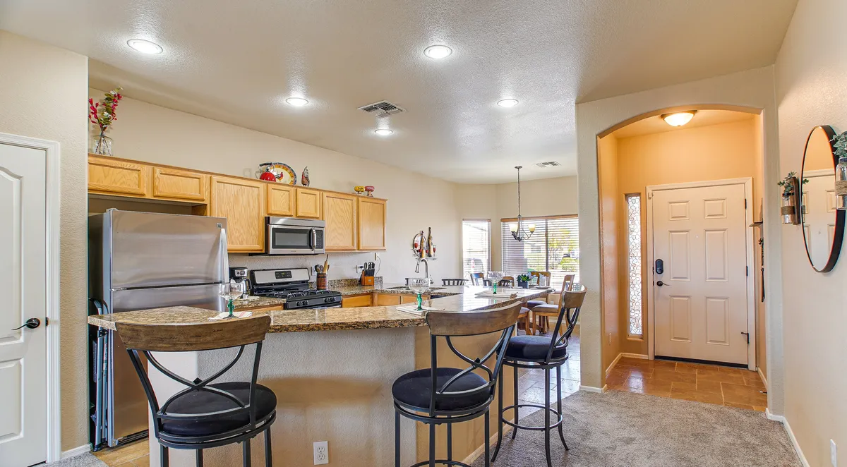 A spacious kitchen featuring a central island with bar stools, sleek stainless steel appliances, and direct sightlines to a stylish adjacent dining area and entryway. The setup is ideal for cooking, entertaining friends, and hosting family gatherings.