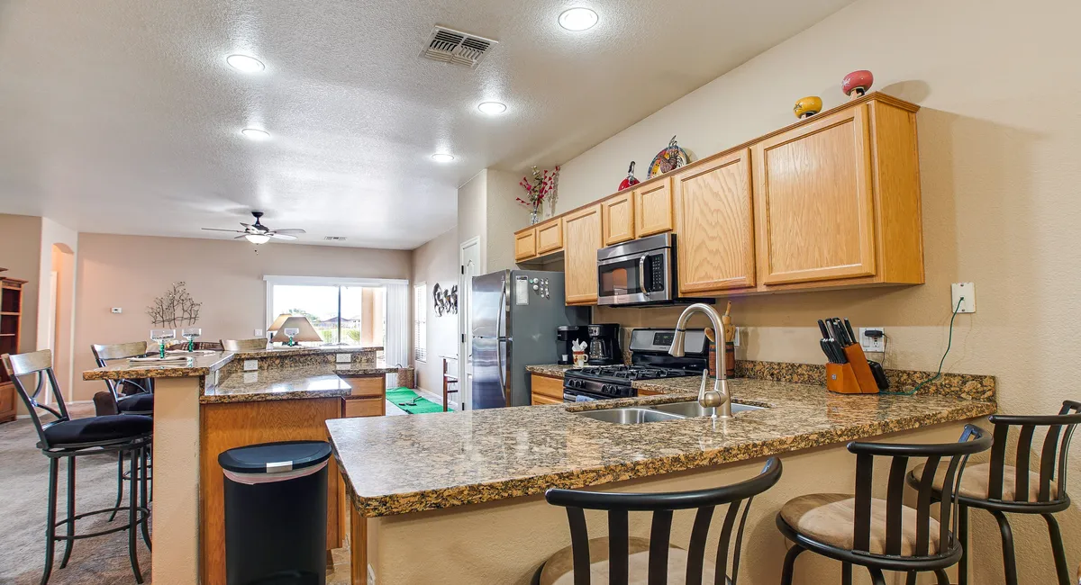 A stylish, modern kitchen interior with a granite countertop, stainless steel appliances, and bar stools. The layout hints at open living spaces and versatile indoor amenities, suitable for casual gatherings and indoor activities.