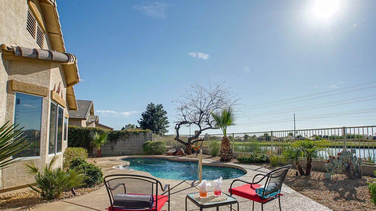 This image shows a sun-drenched swimming pool framed by lounge chairs, decorative cacti, and tall palm trees. The pool area is spacious, with plenty of room for relaxation, sunbathing, and outdoor dining. The inviting turquoise water and lush landscaping create a resort-like atmosphere perfect for families.
