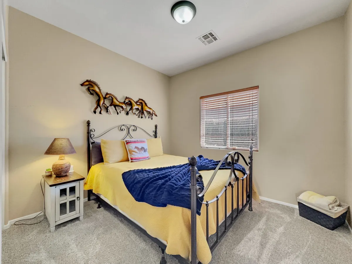 A tastefully styled bedroom with a comfortable bed draped in a blue blanket, horse-themed wall art, and a cozy nightstand. Soft natural light streams through the window, creating an inviting, restful ambiance.