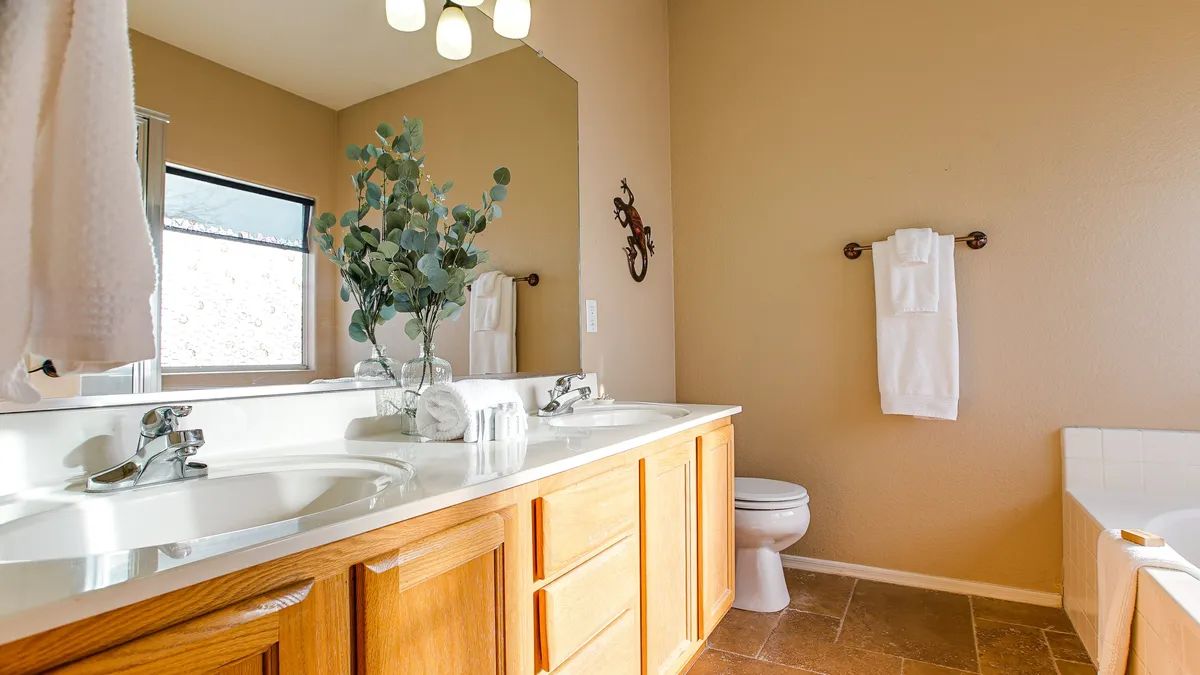 A modern bathroom showcasing a double vanity with elegant mirrors, a potted plant for a touch of greenery, fluffy towels on a rack, and a bathtub for relaxing soaks. The palette is soothing and contemporary.