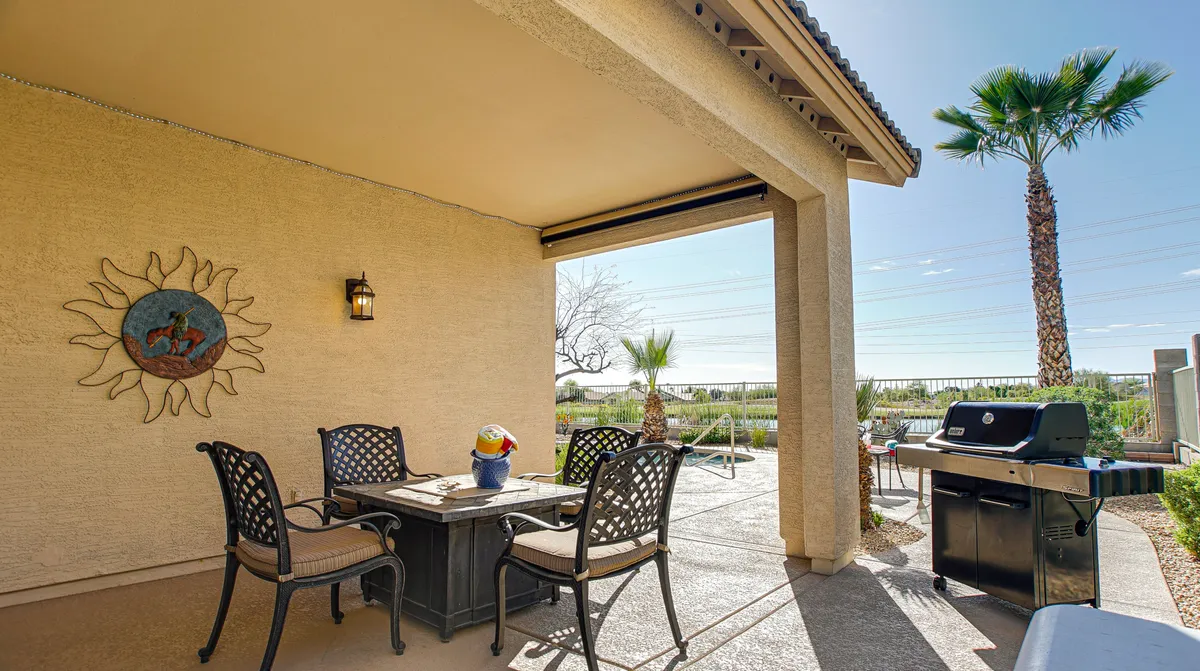 A relaxed outdoor dining area with a table, grill, palm trees, and decorative sun wall art. The space is ideal for al fresco dinners, barbecues, or spontaneous gatherings, with a cheerful and welcoming mood.