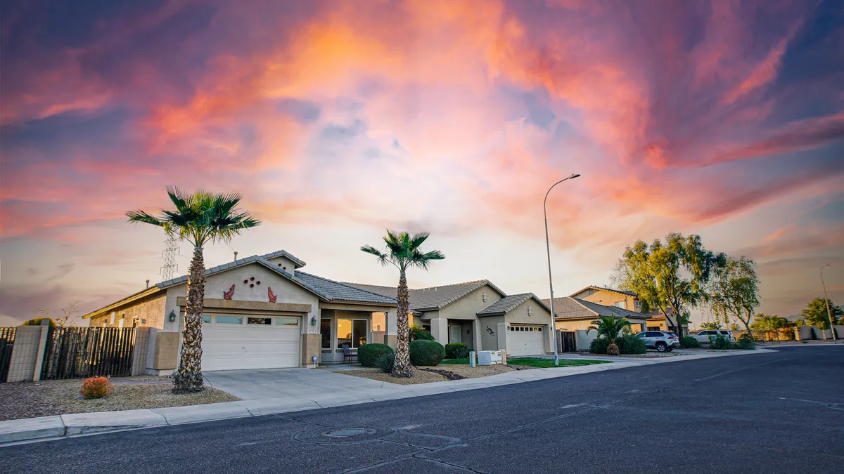 A picturesque neighborhood scene featuring palm trees, neighborhood houses, and a colorful sunset sky. The inviting landscape is perfect for evening strolls or gathering under the palm trees, evoking the warmth and friendliness of the area.